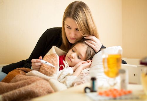 Young mother checking temperature of sick daughter lying in bed